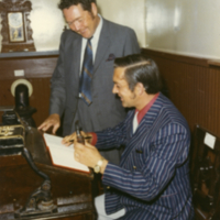 Un homme signe un livre en compagnie d'un autre homme